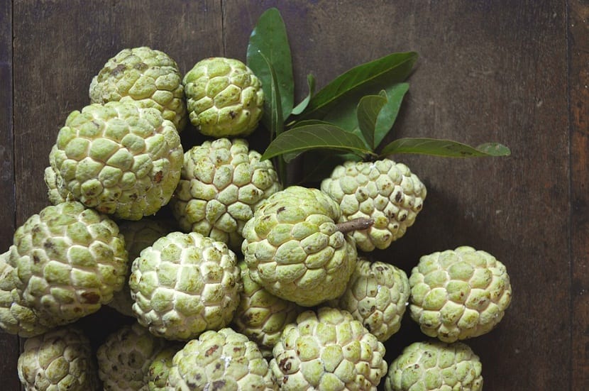 varias chirimoyas de color verde con sus hojas encima de una mesa